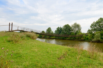 Old suspension bridge over the river on a cloudy summer day