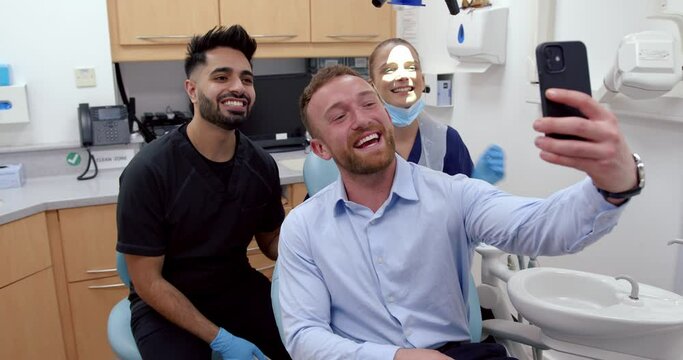 caucasian male patient taking selfie with male and female doctors showing new clean teeth