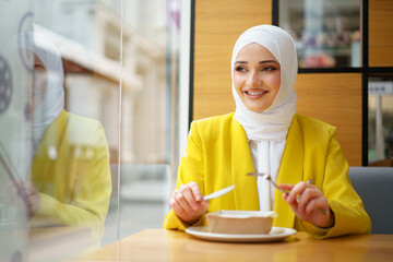 Young muslim woman in hijab having a lunch in cafe