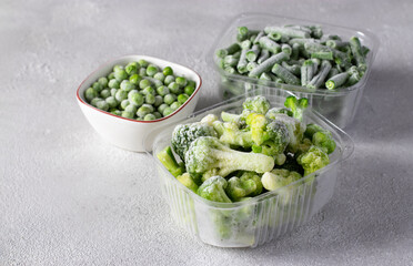 Frozen vegetables such as green peas, green beans and broccoli in the storage boxes on the light gray background.