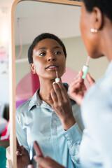 A beautiful young African American woman is applying makeup in front of a mirror.