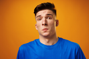 Portrait of crazy amazed young man in blue t-shirt against yellow background