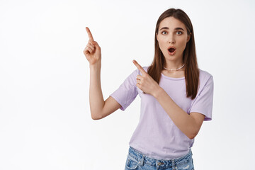 Impressed young woman pointing left, show way and gasp amazed, intrigued by banner or promo deal, asks question about product, white background