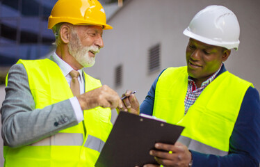   Mature engineer discussing the structure of the building with architects colleague at construction site. Engineers with document.