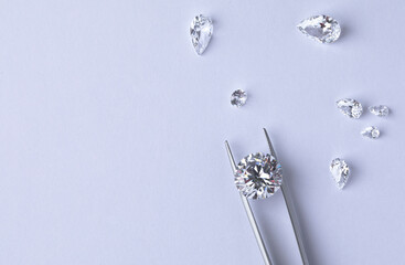 Polished diamonds of various sizes and shapes wit jewelry tools lie at the workplace of an expert examining the quality of stones on light background with copy space. High quality photo - obrazy, fototapety, plakaty