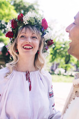 Young people are posing in traditional folk costumes. Cossacks man and woman in wreaths and embroidered shirts. Reconstruction of vintage traditions and customs. Guy and girl kiss