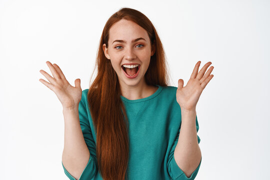 Image of happy beautiful girl with red hair, clap hands and laughing joyful, enjoying watching funny and amusing event, standing over white background