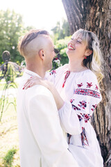Young people are posing in traditional folk costumes. Cossacks man and woman in wreaths and embroidered shirts. Reconstruction of vintage traditions and customs. Guy and girl kiss