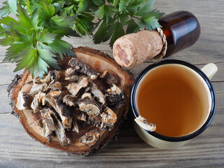 Root, herbal tea in a mug, drink in a bottle and spicy herb lovage with green leaves in a wooden...