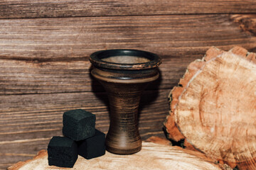 An earthenware bowl for a hookah with coconut coals stands on a wooden background.