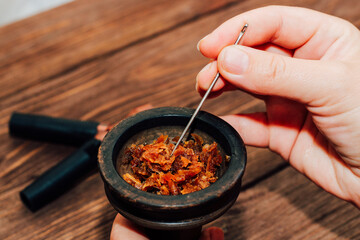 Clay bowl for hookah with coconut coals, wooden mouthpieces on a wooden background top view. Girl fills smoking tobacco.