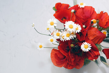 A bouquet of wildflowers: daisies and poppies in a transparent glass vase on a gray background.