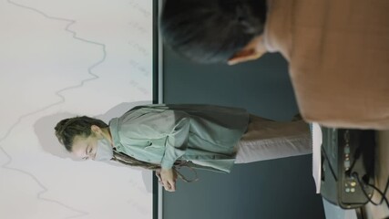 Vertical slowmo tracking of young woman with dreadlocks wearing face mask and delivering financial presentation to team of colleagues in office - Powered by Adobe