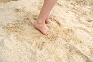 child's bare feet in the sand, boy plays in the summer with sand on the playground, in the sandbox, the concept of building sand castles, summer vacation, fun on the beach