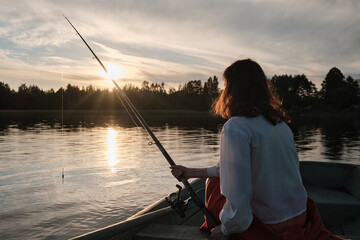 Girl is fishing with a fishing rod. Girl is sitting in the boat