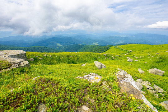 view from runa mountain. huge stones on the grassy slopes. summer landscape of carpathian mountains. bieszczady and vihorlat ridge in the distance beneath a sky low clouds