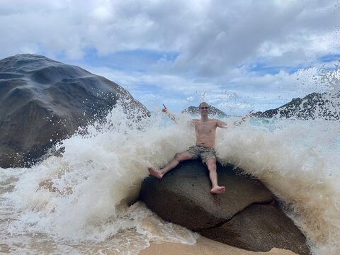 Jeune homme devant des rochers granitique devant la mer agitée
