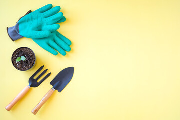 composition of gardening tools and green gloves on yellow background.
