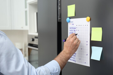 Man checking to do list on fridge in kitchen, closeup - obrazy, fototapety, plakaty