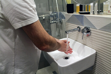 A man washes his hands with water in the bathroom sink. The concept of an attentive attitude to cleanliness and one's health. The importance of hygiene in the context of the coronavirus pandemic.