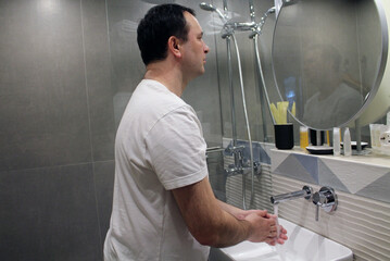 A man washes his hands with water in the bathroom sink. The concept of an attentive attitude to cleanliness and one's health. The importance of hygiene in the context of the coronavirus pandemic.