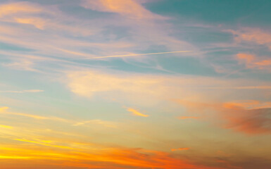 Sunset sky with condensation trail. Texture of bright evening sky during sunset. Dramatic blue and orange, colorful clouds at twilight time. Abstract weather nature background.