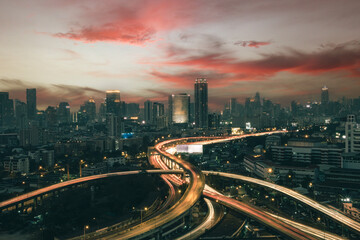 Obraz na płótnie Canvas Aerial view of the modern buildings finance and highway at night of Bangkok cityscape, Thailand. Car lights at evening on the road going fast to the city. The speed traffic trails on motorway rooftop.