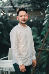 Fototapeta premium Portrait of a casually dressed handsome young Asian man smiling while standing alone outside on garden.