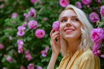 Happy smiling beautiful blonde woman posing in blooming rose garden. Copy, empty space for text