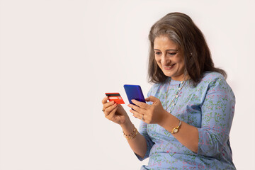 A HAPPY ADULT WOMAN USING DEBIT CARD TO DO ONLINE TRANSACTIONS ON MOBILE