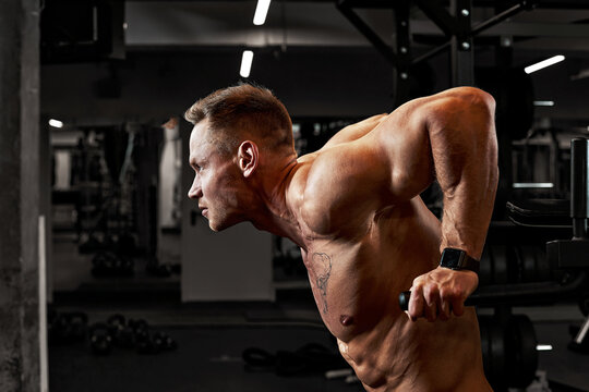A man with sports aggression doing press on the uneven bars in a gym, training pectoral muscles and triceps