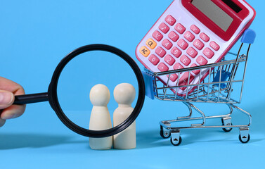 miniature metal shopping cart with calculator and wooden family. Hand with a magnifying glass
