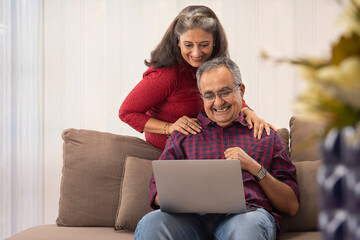 A HUSBAND AND WIFE HAPPILY USING LAPTOP FOR VIDEO CALLING - obrazy, fototapety, plakaty