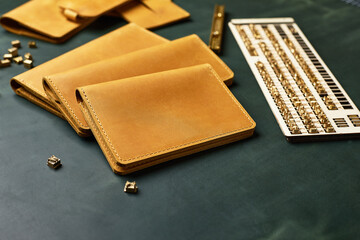 A set of wallets, business card holders and key holders made of handmade leather, yellow with a piece of green leather surrounded by tools, demonstration of handmade leather products