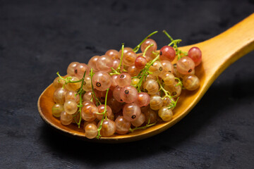 White currants in a wooden spoon on a black background. Lots of ripe white currants. Delicious berry.