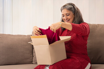 A SENIOR ADULT WOMAN HAPPILY OPENING A COURIER BOX WITH DRESS IN IT