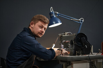A tanner or skinner sews leather on a special sewing machine, side shot, blue background, a worker sews on a sewing machine.