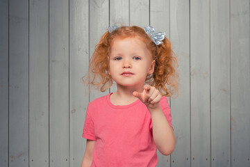 cute redhead little girl pointing at camera, standing in pink casual t shirt, picking or choosing, inviting people