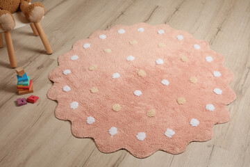 Round pink rug with polka dot pattern and toys on wooden floor in baby's room