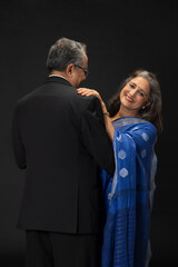 A HAPPY WIFE LOOKS AT CAMERA WHILE STANDING WITH SUPPORT OF HUSBAND