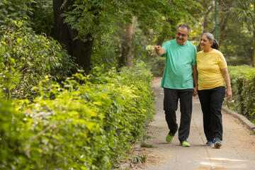 A SENIOR ADULT HUSBAND POINTING TOWARDS GARDEN WHILE WALKING WITH WIFE