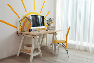 Stylish home office interior with comfortable workplace and sun art on wall