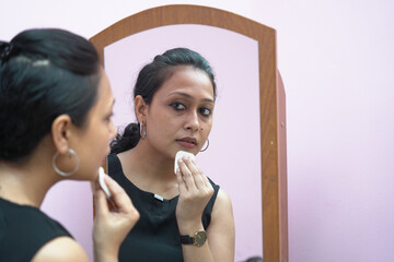 A lady in 30s putting make up in front of a mirror