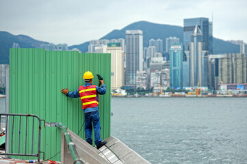 Construction worker erects a fence on the embankment 