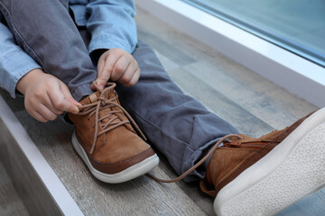 Little boy tying shoe laces at home, closeup