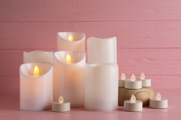 Fototapeta na wymiar Glowing decorative LED candles on pink wooden background