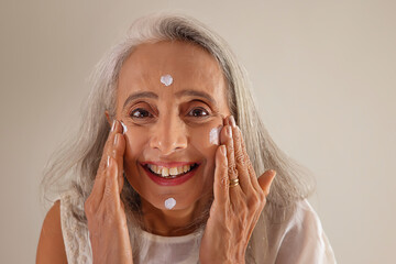 An old beautiful woman applying  face cream .