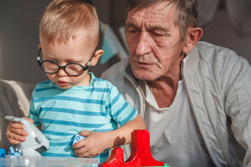Elderly grandfather plays with little grandson with plastic blocks