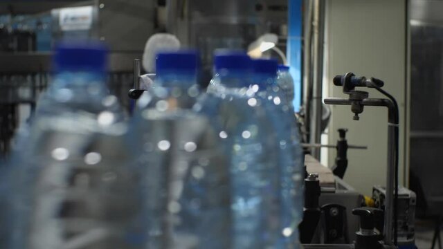 Blurry video close-up of blue plastic mineral water bottles moving on a conveyor belt. Production of drinking water at a food processing plant