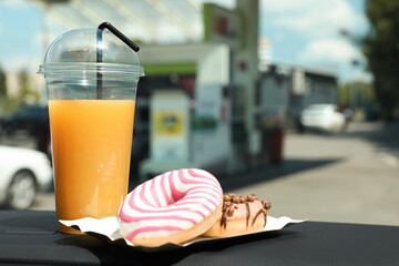 Plastic cup of juice and doughnuts on car dashboard at gas station. Space for text